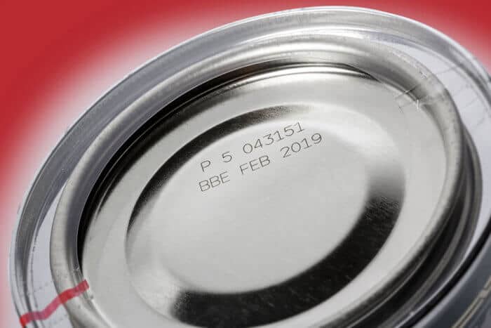 Metal can lid with manufacturing details and expiration date focus on food packaging and safety.
